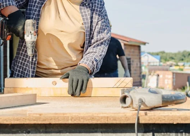 Un hombre usando un taladro sobre una mesa de madera.
